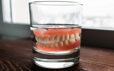 A denture in a glass of water. Dental prosthesis care. Full removable plastic denture of the jaws