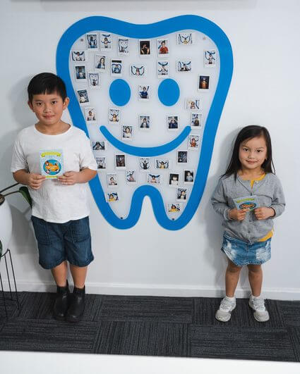 Kids holding awards at dental clinic wall display.