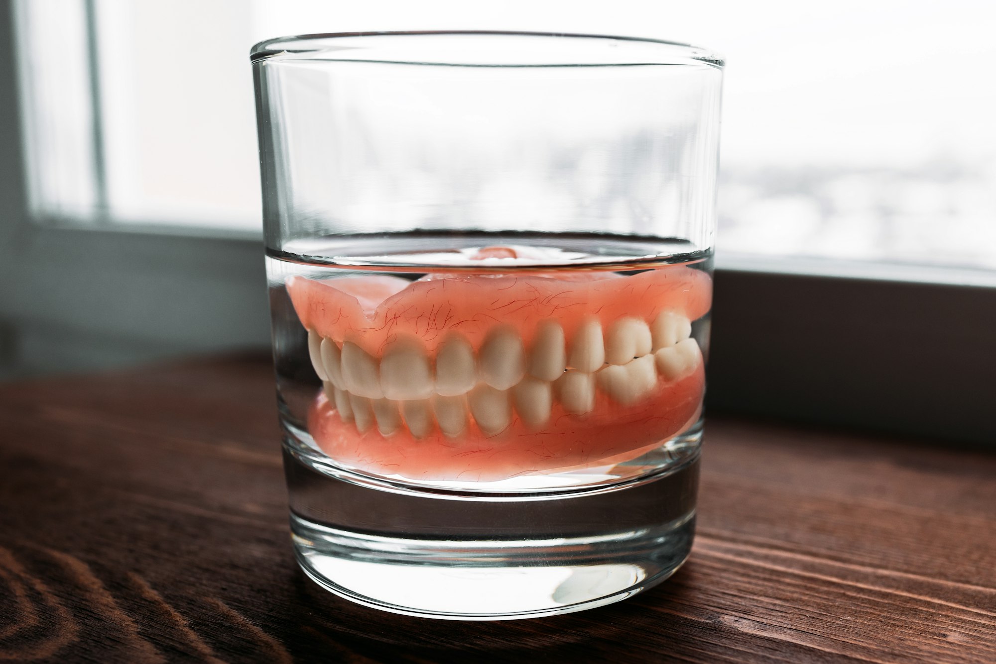 Dentures in glass on wooden table