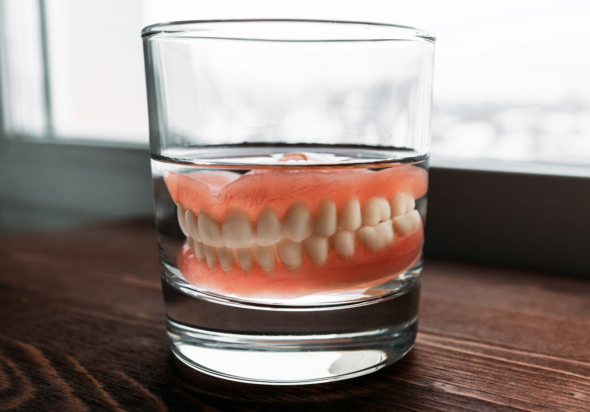 A denture in a glass of water. Dental prosthesis care. Full removable plastic denture of the jaws