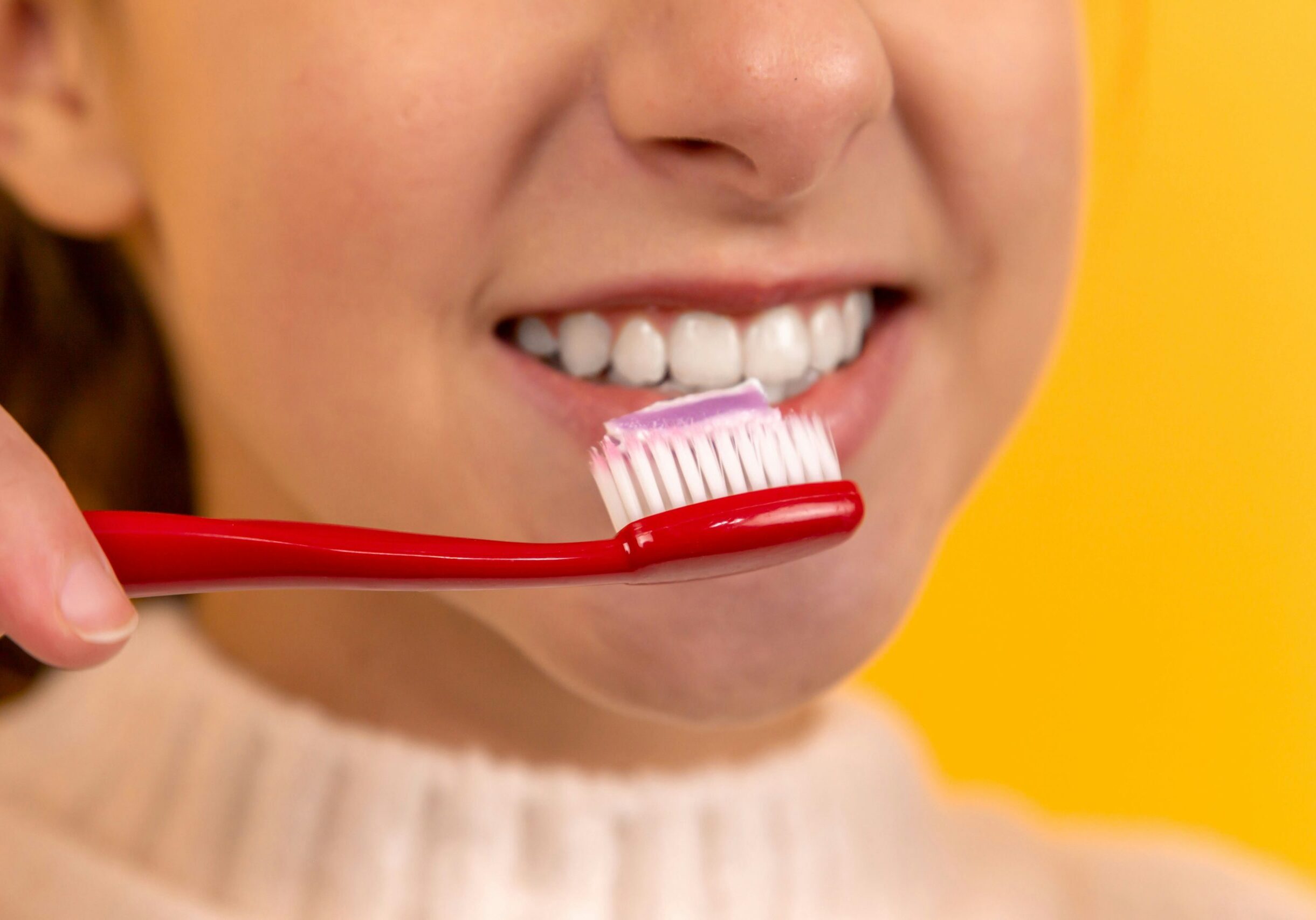 a woman brushing her white teeth with a red toothbrush