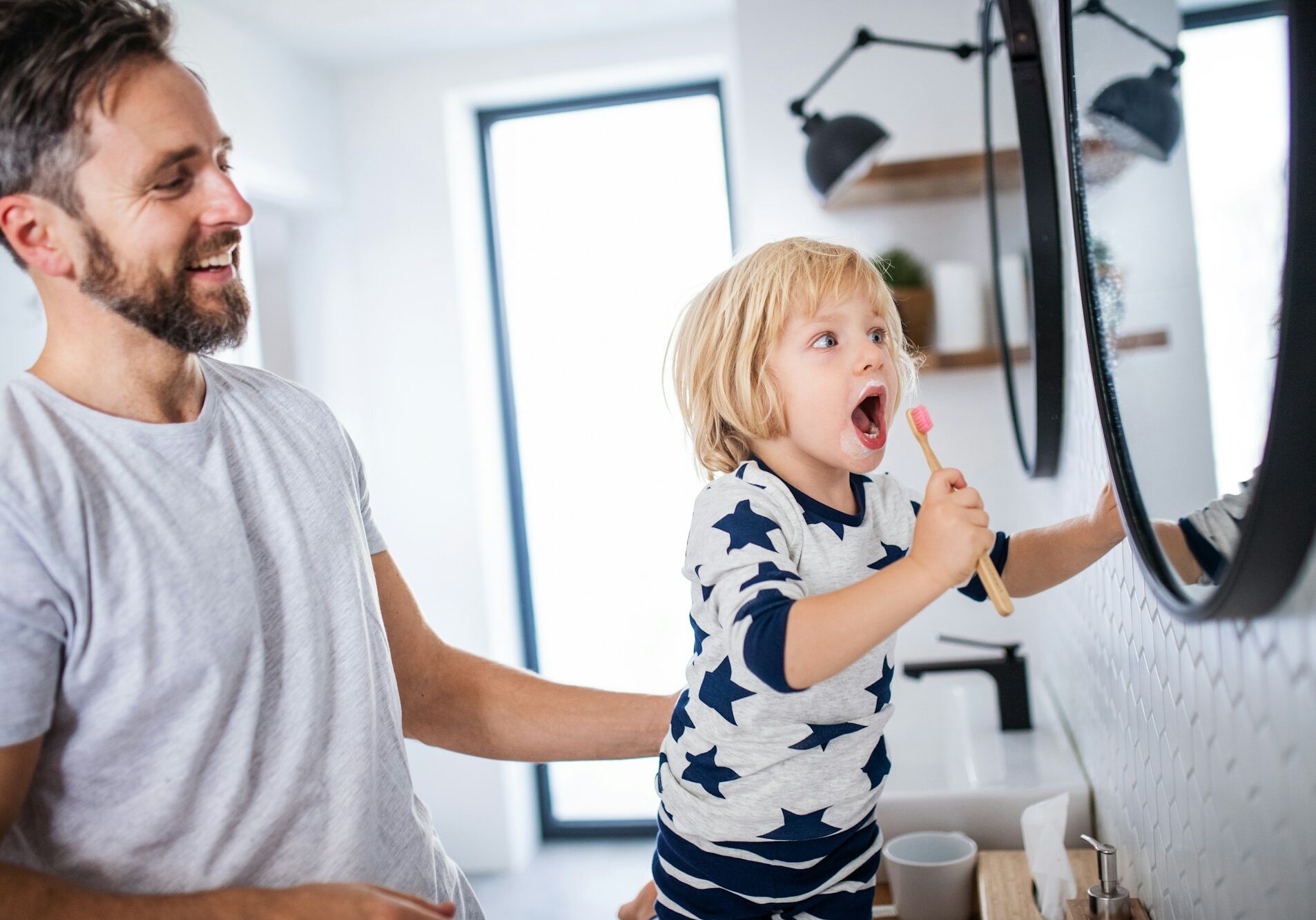 Mature father with small son indoors in bathroom, brushing teeth.