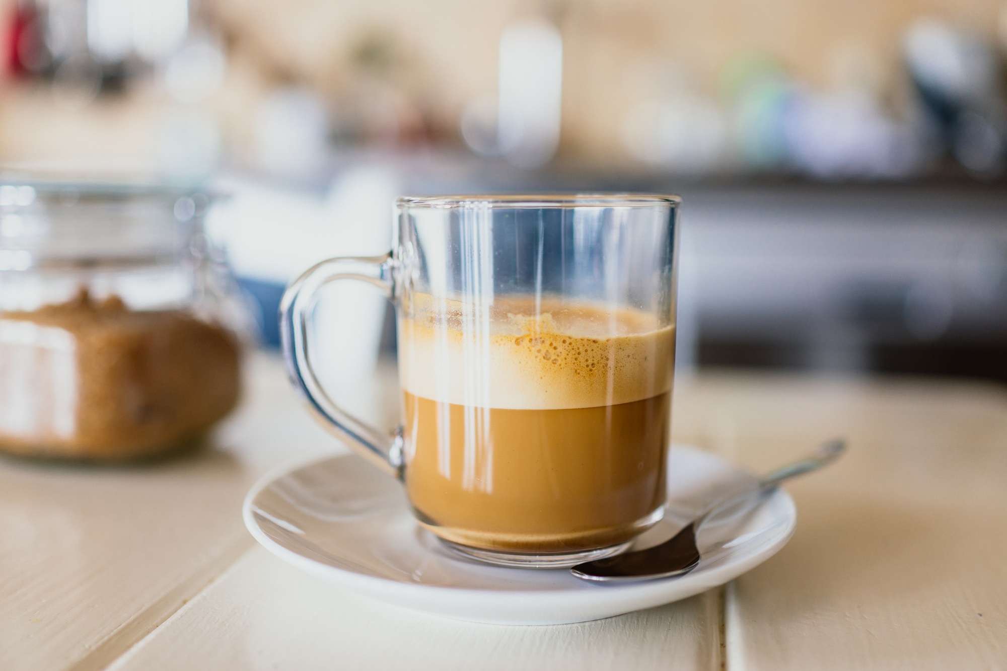 Glass of creamy coffee on saucer with spoon.