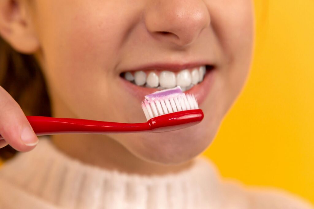 a woman brushing her white teeth with a red toothbrush