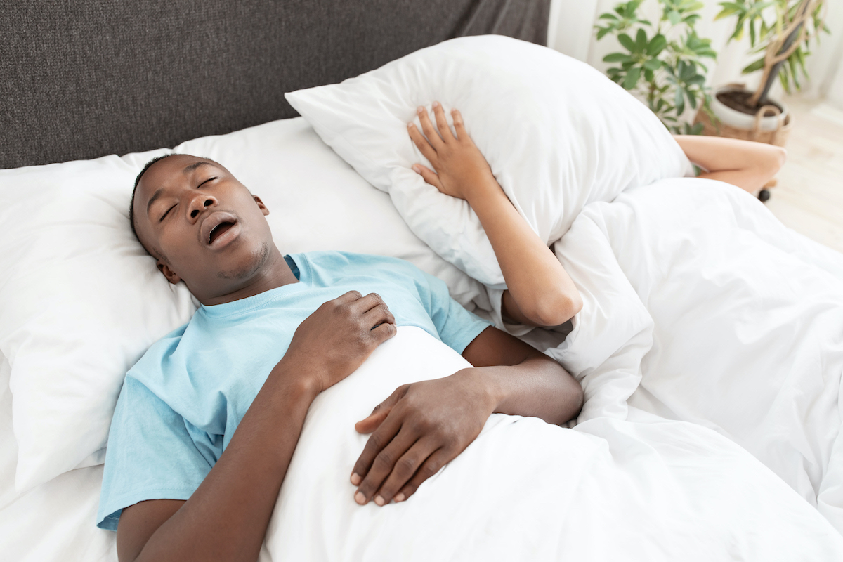 Person snoring in bed, partner covers ears.