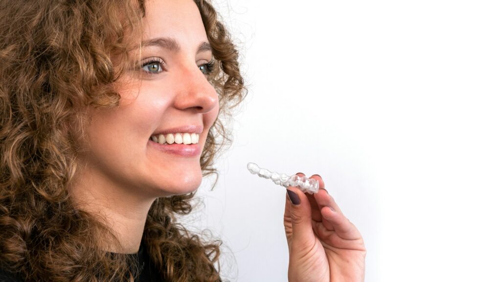 Smiling beautiful adult woman holds invisalign transparent braces in her hand