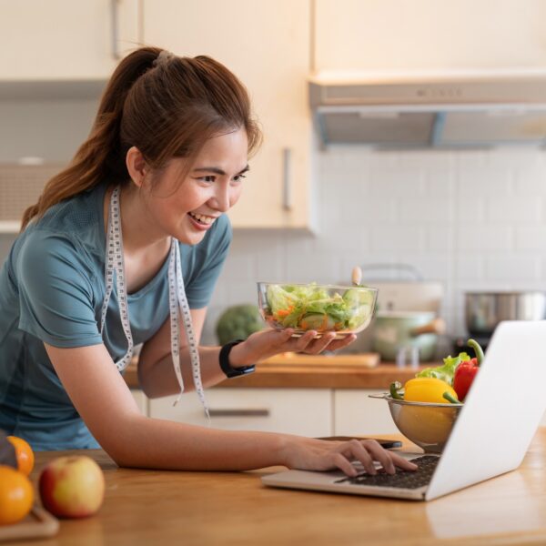 Woman cooking salad using laptop in modern kitchen.
